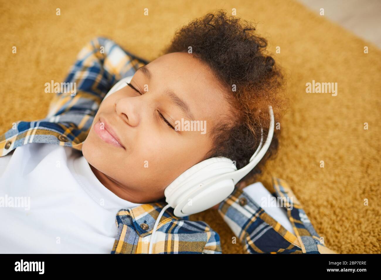 Porträt eines Jugendlichen afrikanischen Jungen mit Kopfhörern und liegen auf dem Boden, während Musik mit geschlossenen Augen genießen, kopieren Raum Stockfoto