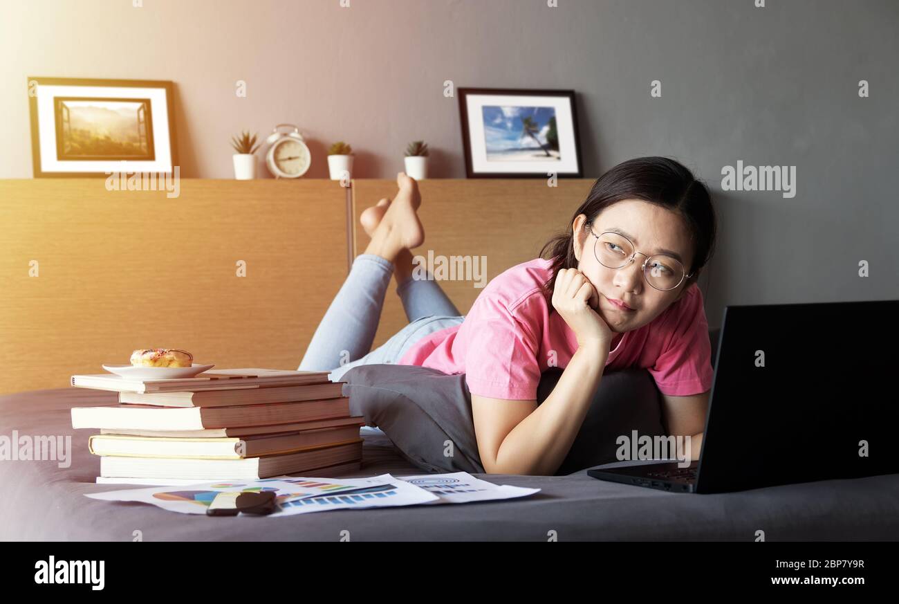 Arbeiten von zu Hause, neue normale Konzept. Frau arbeitet mit Laptop-Computer auf dem Bett aus ihrem Zimmer während der Selbstisolierung, Gefühl gelangweilt Stockfoto