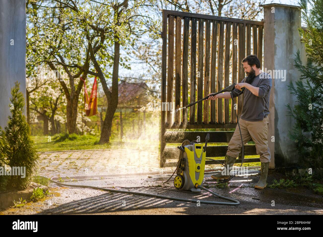 Ein Mann mit mittlerer Erwachsener, der ein Holztor mit einer Waschmaschine reinigt. Hochdruckwasserreiniger verwendet, um DIY Reparatur Gartentor. Stockfoto