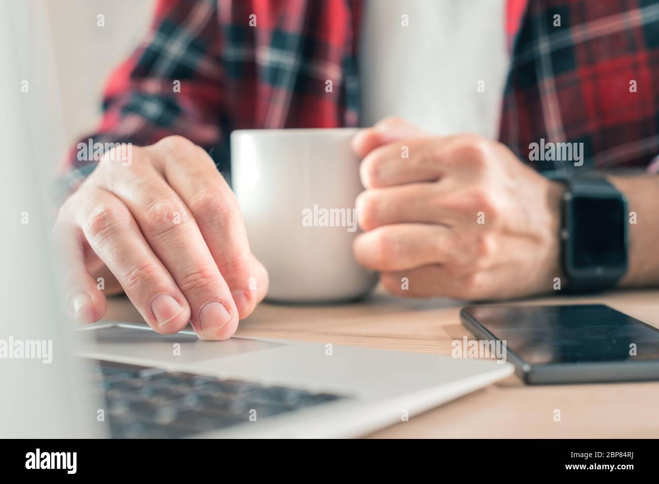 Freiberuflicher Mitarbeiter, der Laptop-Computer verwendet und Kaffee im Home Office trinkt, selektiver Fokus auf Hände Stockfoto