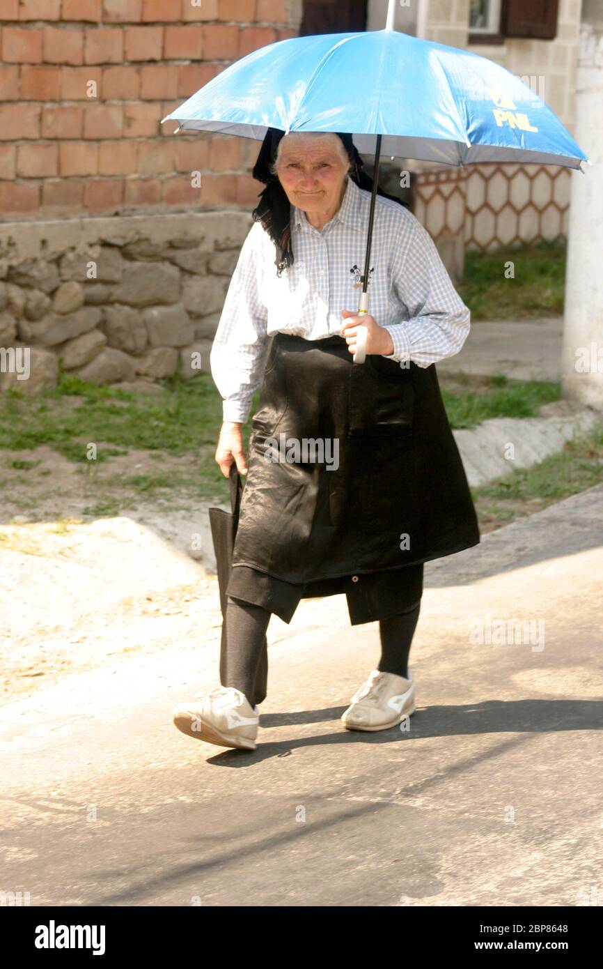 Sibiu County, Rumänien. Alte Frau, die auf der Straße geht und mit einem Sonnenschirm vor der Sonne schützt. Stockfoto
