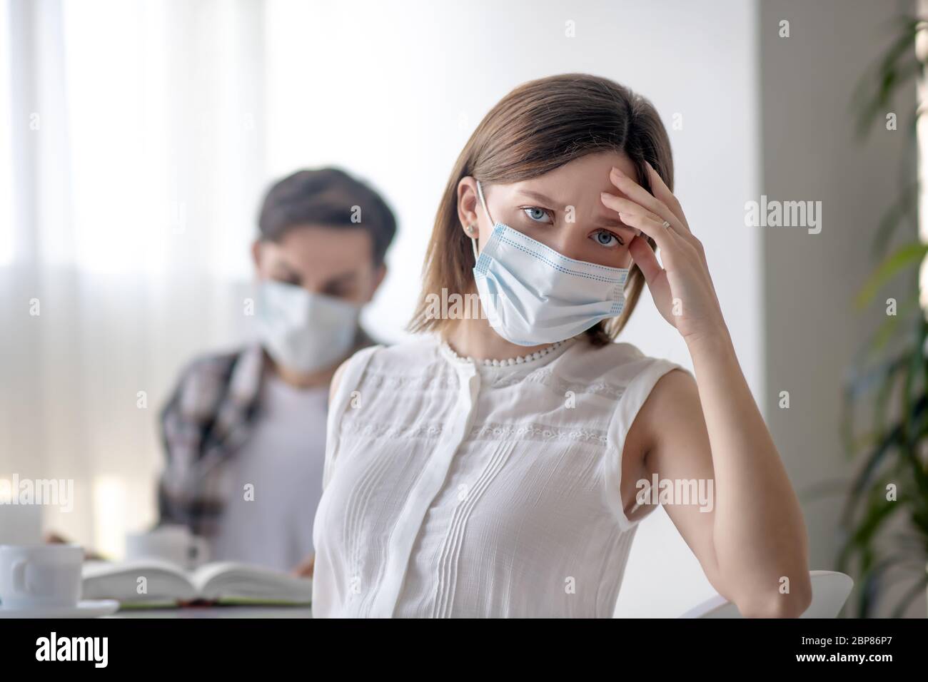 Junge Frau in einer Gesichtsmaske mit Kopfschmerzen Stockfoto