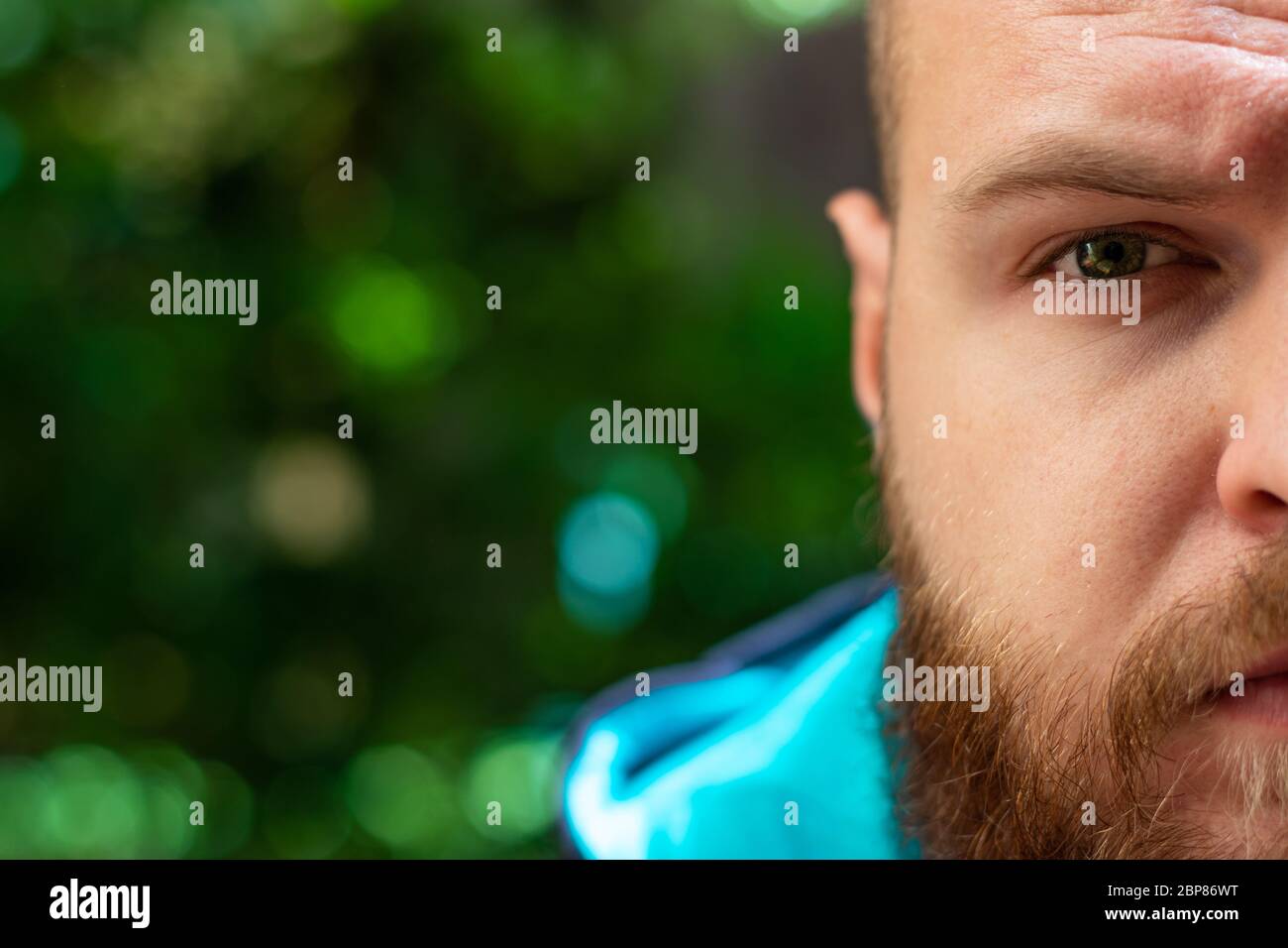 Halbkopf eines kahlen bärtigen Mann sichtbar, grün ernst traurigen Auge im Fokus auf grünen Wald Hintergrund scheint. Stockfoto