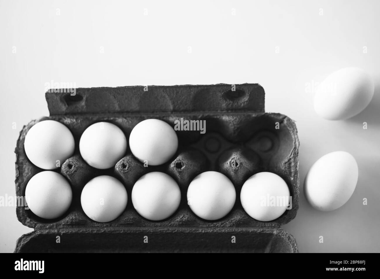 Ein Schwarz-Weiß-Bild von weißen Hühnereiern, die in einer dunklen Pappschachtel aus dem Laden auf einem weißen Tisch stehen. Stockfoto