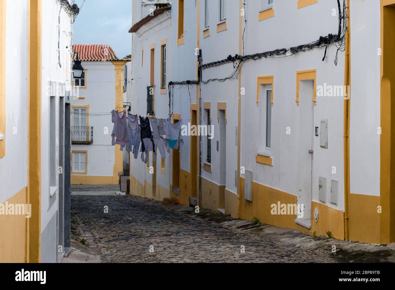 Gepflasterte Gasse zwischen weiß getünchten Hauswänden mit Farbakzenten und Wäsche, die in der traditionellen Nachbarschaft an den Linien trocknen kann Stockfoto