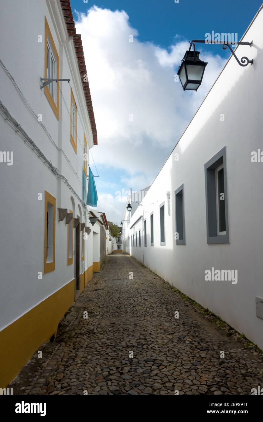 Gepflasterte Gasse zwischen weiß getünchten Hauswänden mit Farbakzenten in einem traditionellen Viertel in der historischen Altstadt von Evora in Port Stockfoto
