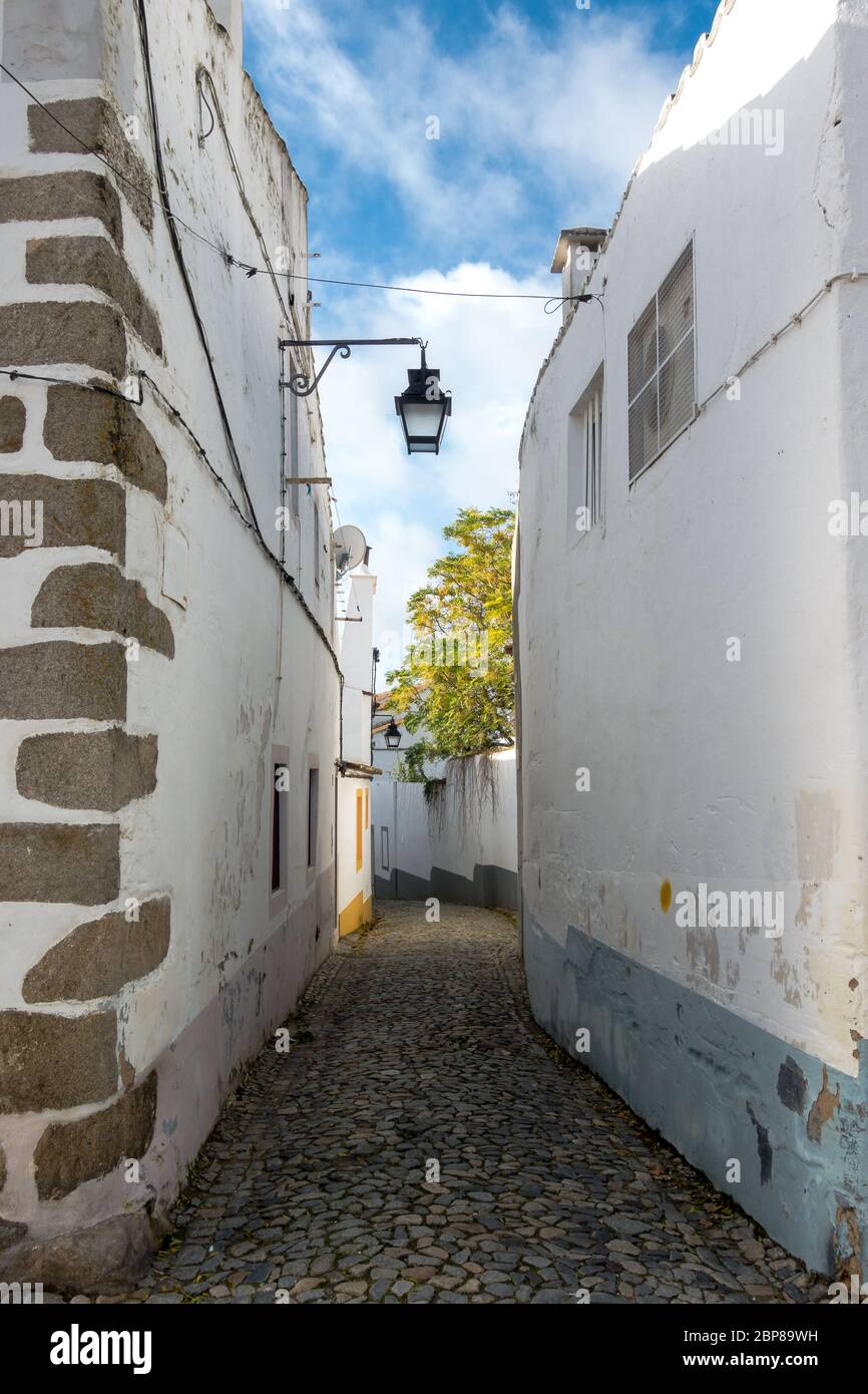 Gepflasterte Gasse zwischen weiß getünchten Hauswänden mit Farbakzenten in einem traditionellen Viertel in der historischen Altstadt von Evora in Port Stockfoto