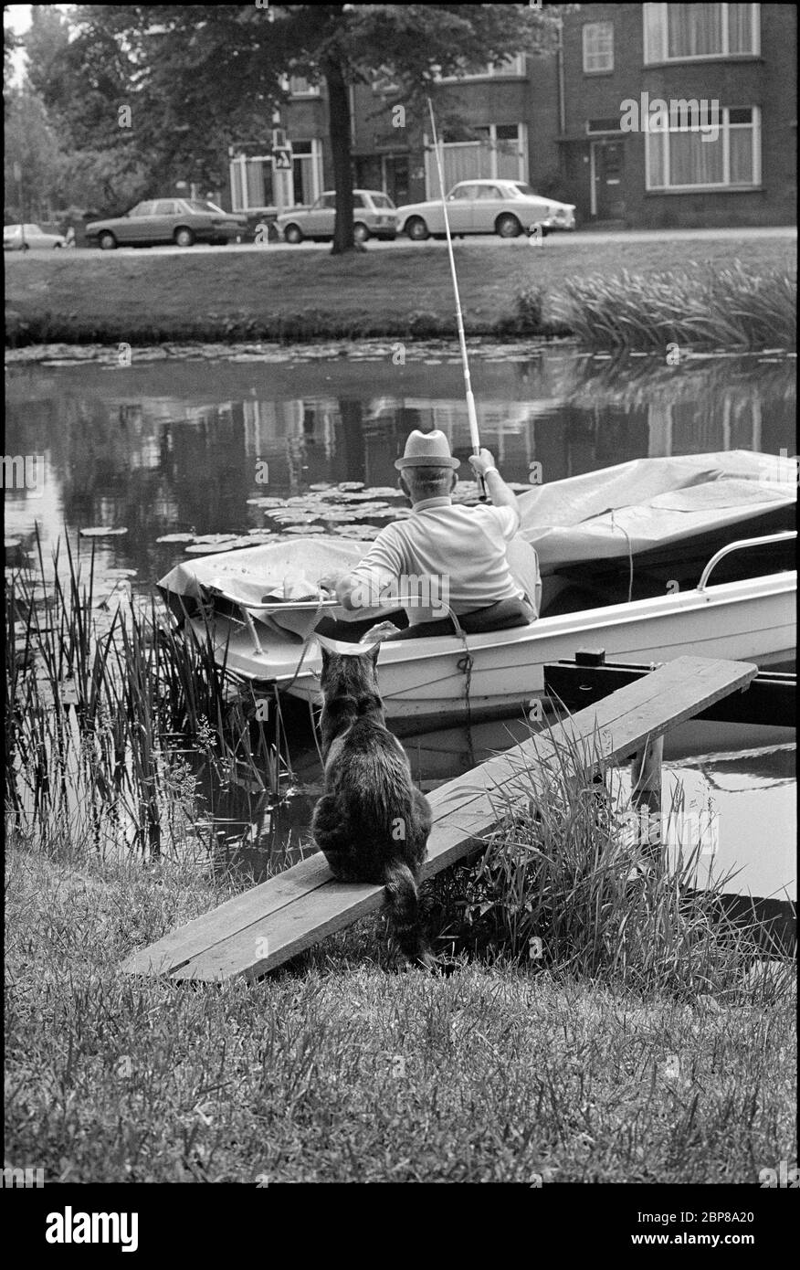 Historisches Schwarz-Weiß-Bild eines Fischers und einer wartenden Katze im Jahr 1977, Leiden, Niederlande Stockfoto