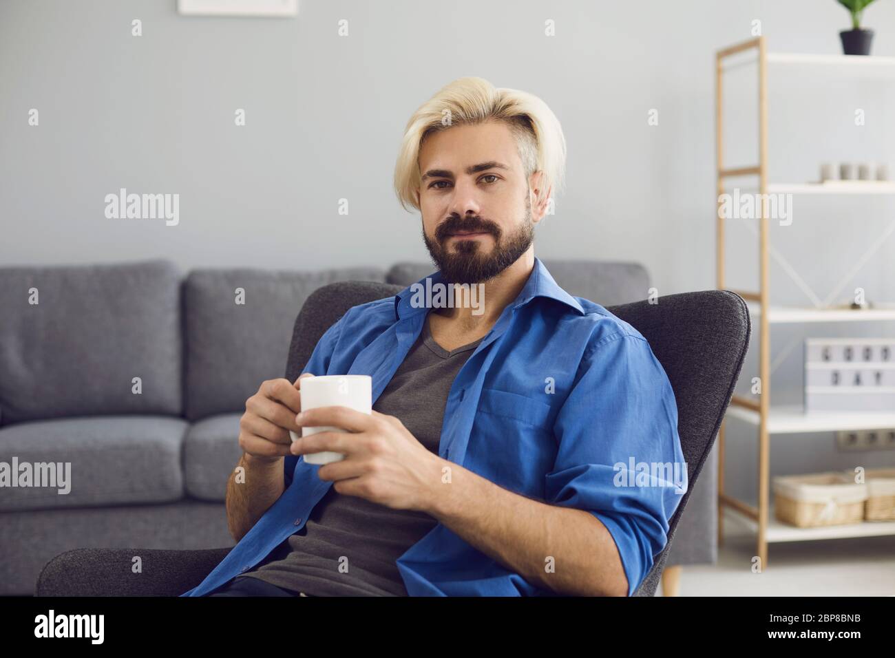 Online-Video-Chat. Ein junger Mann mit einer Tasse Kaffee schaut in einem Wohnzimmer auf die Kamera. Stockfoto