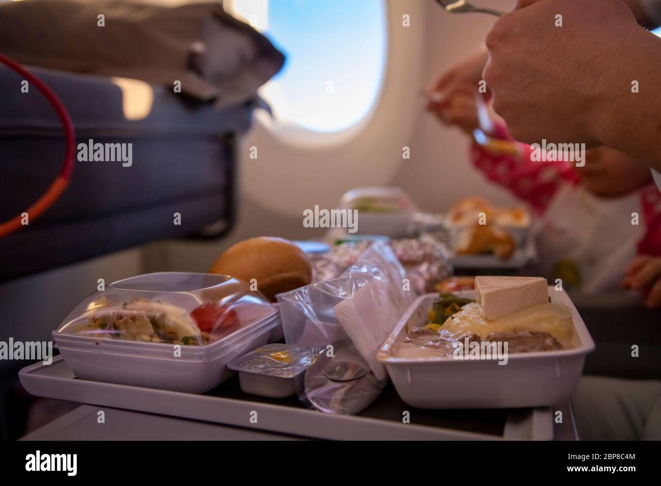 Nahaufnahme Passagierflugzeug isst leckere warme Mahlzeit an Bord auf einem Klapptisch. Im Hintergrund ist ein Fenster im Bullauge. Stockfoto