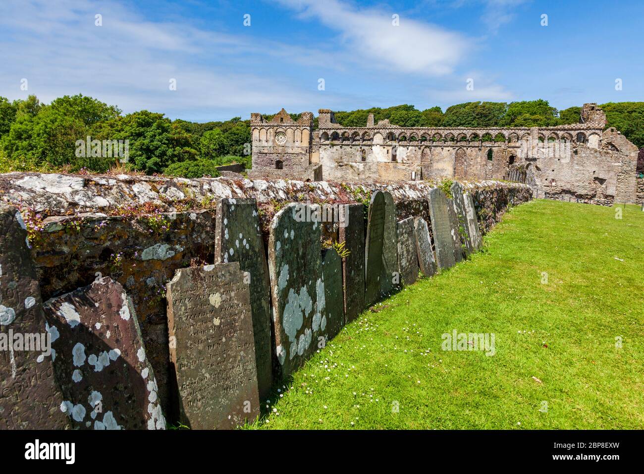 Verwitterte Grabsteine an der Außenmauer zur Saint David's Cathedral mit dem Bischofspalast im Hintergrund, Pembrokeshire, Wales Stockfoto