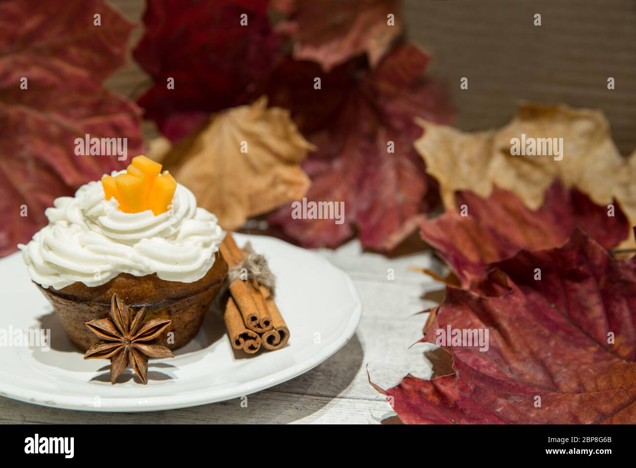 Kürbis-Cupcake mit Gewürzen und Nüssen, verziert mit Kürbisstreifen, geschmolztem Frischkäse und getrockneten Herbstblättern, gelb, rot und orange. Stockfoto
