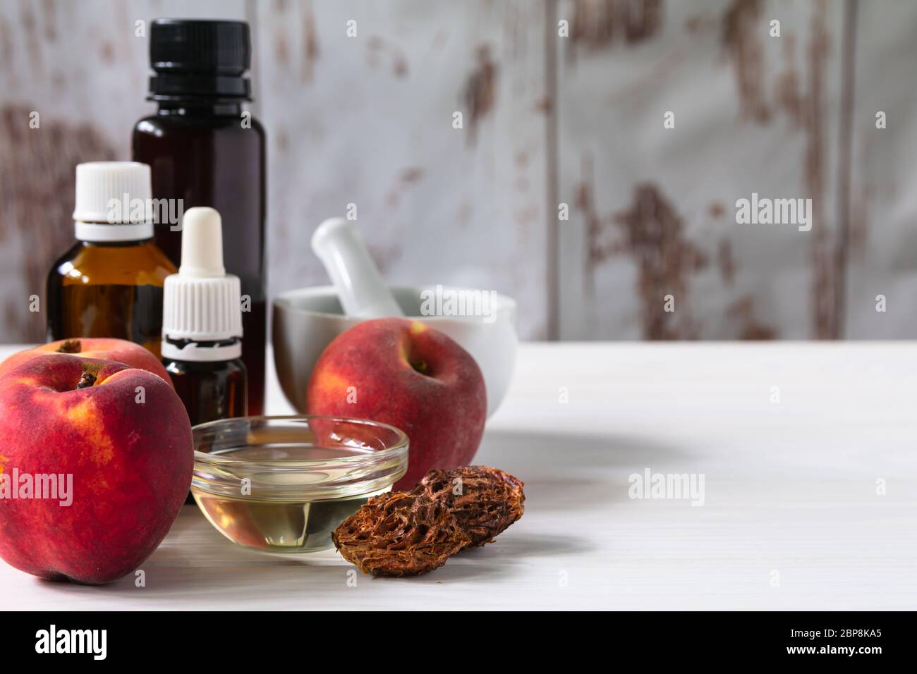 Naturkosmetik Konzept, Pfirsiche mit Glasflaschen mit Öl und Mörtel, auf weißem Holzhintergrund, Kopierraum Stockfoto