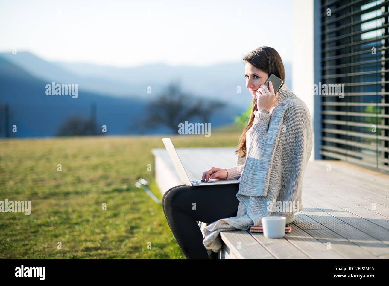 Frau mit Laptop und Smartphone arbeitet im Freien zu Hause, Quarantäne-Konzept. Stockfoto