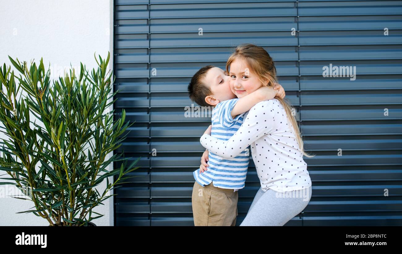 Kleines Mädchen und Junge stehen draußen zu Hause, umarmen. Stockfoto