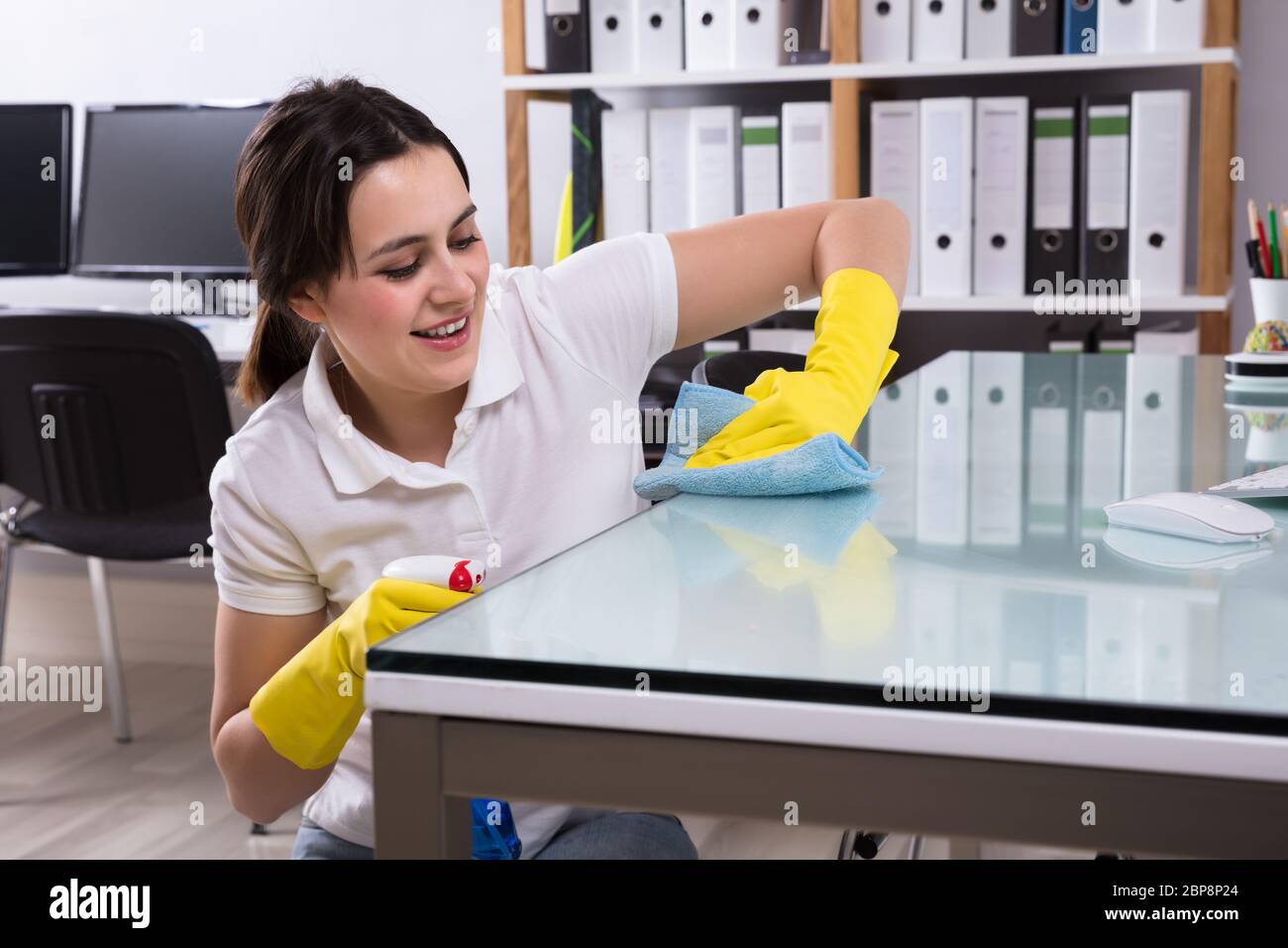 Nahaufnahme einer Lächelnden jungen Frau Reinigung der Glas Schreibtisch mit Rag im Büro Stockfoto