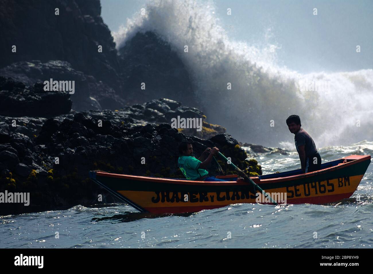 Wave stürzt hart auf den Felsen mit Fischern auf seinem Boot Stockfoto