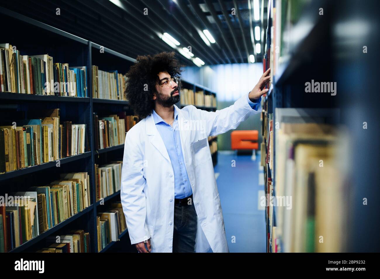 Doktor, der in der Bibliothek steht, auf der Suche nach einem Buch im Regal. Stockfoto