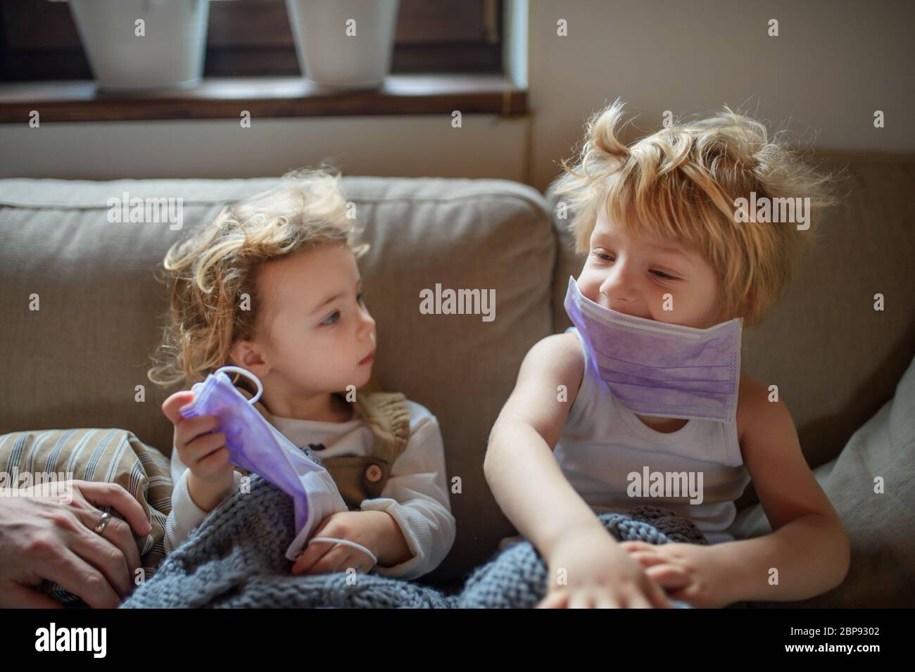 Zwei kleine kranke Kinder mit Gesichtsmaske zu Hause sitzen auf dem Sofa. Stockfoto