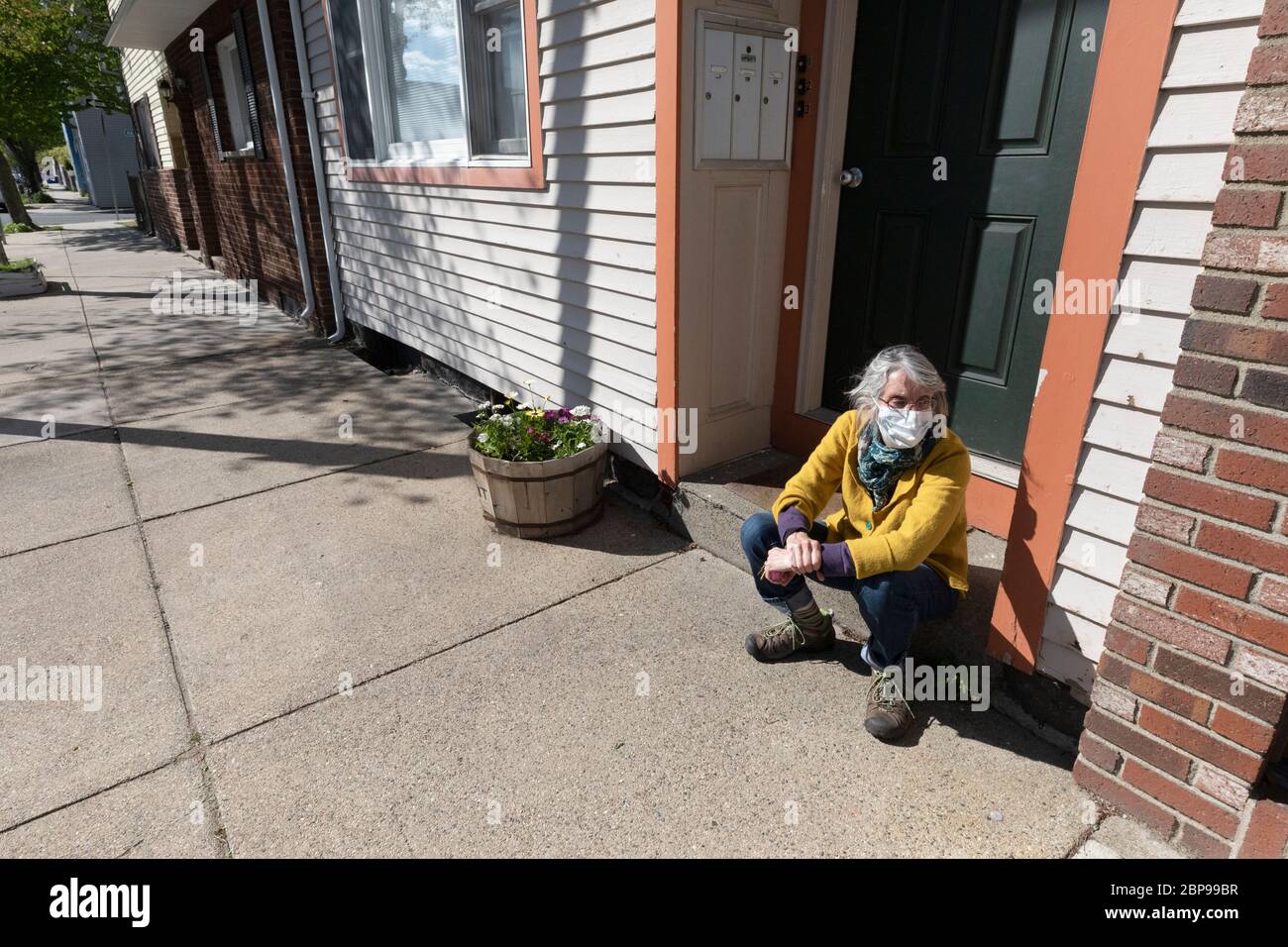 Frau mit Schutzmaske sitzt auf der vorderen Treppe des Wohnhauses, Boston Massachusetts USA Stockfoto