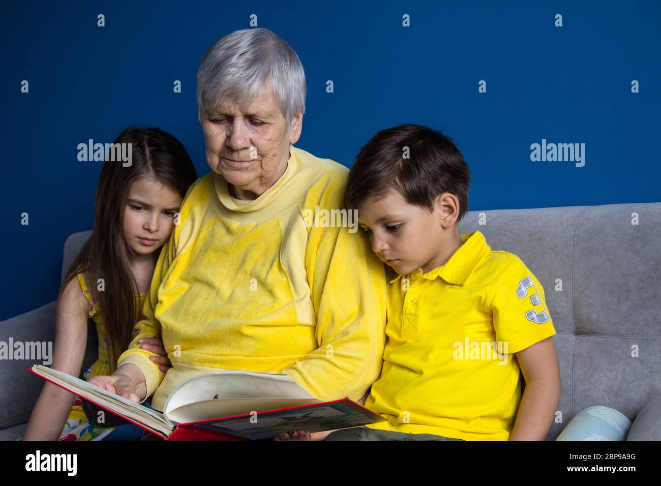 Eine alte Großmutter und ihre geliebten Enkelkinder sitzen zu Hause und lesen ein Interessantes Buch Stockfoto
