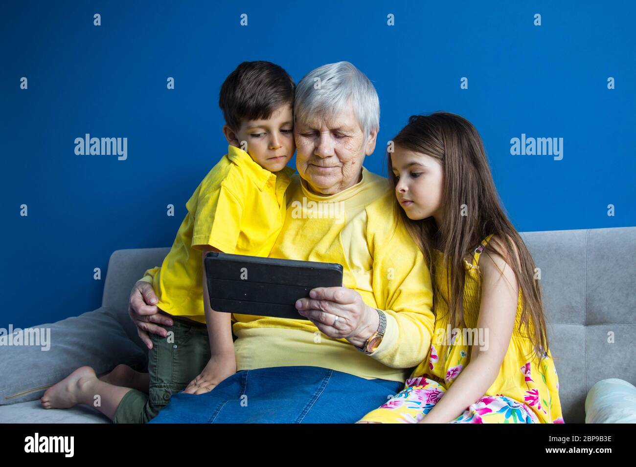 Eine alte Großmutter und ihre geliebten Enkelkinder sitzen zu Hause und telefonieren Stockfoto