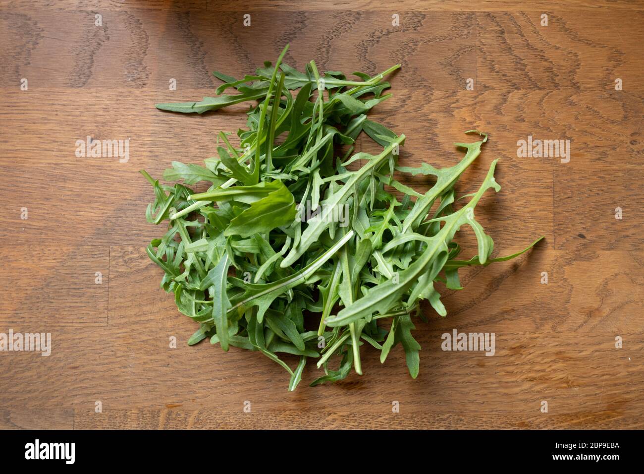 Rucola auf Tisch liegend, Flachlage von oben geschossen, brauner Küchentisch Stockfoto