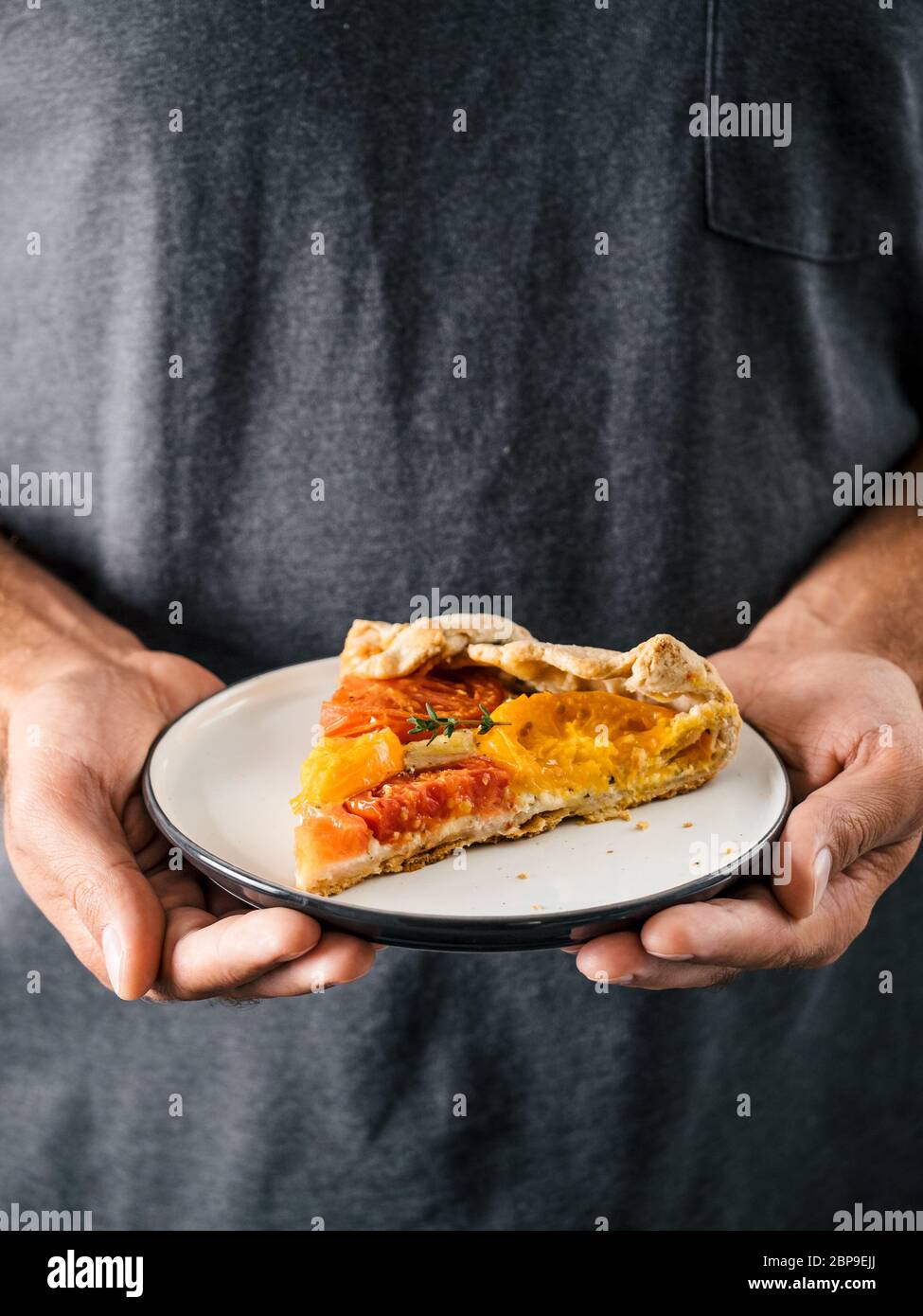 Hände nimmt Teller mit Portion Stück Kuchen. Herzhafte, frisch hausgemachte Tomatentorte oder Galette. Gesunde Vorspeise - Vollkorn oder Roggen-Weizen-Kuchen mit Toma Stockfoto