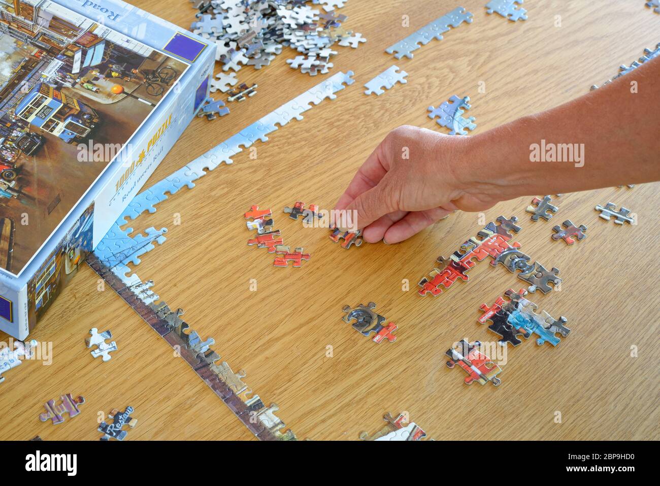 Puzzle wird von einer Frau wieder zusammengebaut. Referenzbild zu Hand und Kanten fast vollständig. Stockfoto