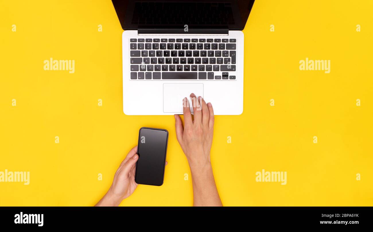 Laptop, Frau weibliche kaukasische Hände hängen Handy auf gelbem Hintergrund Stockfoto