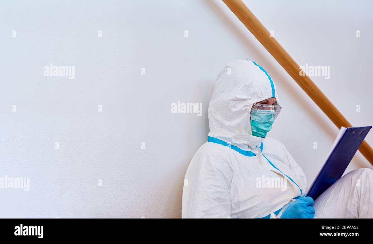 Pflegepersonal in der Klinik in Schutzkleidung Studien Liste auf dem Klemmbrett während der Pause auf dem Boden während Coronavirus-Epidemie Stockfoto