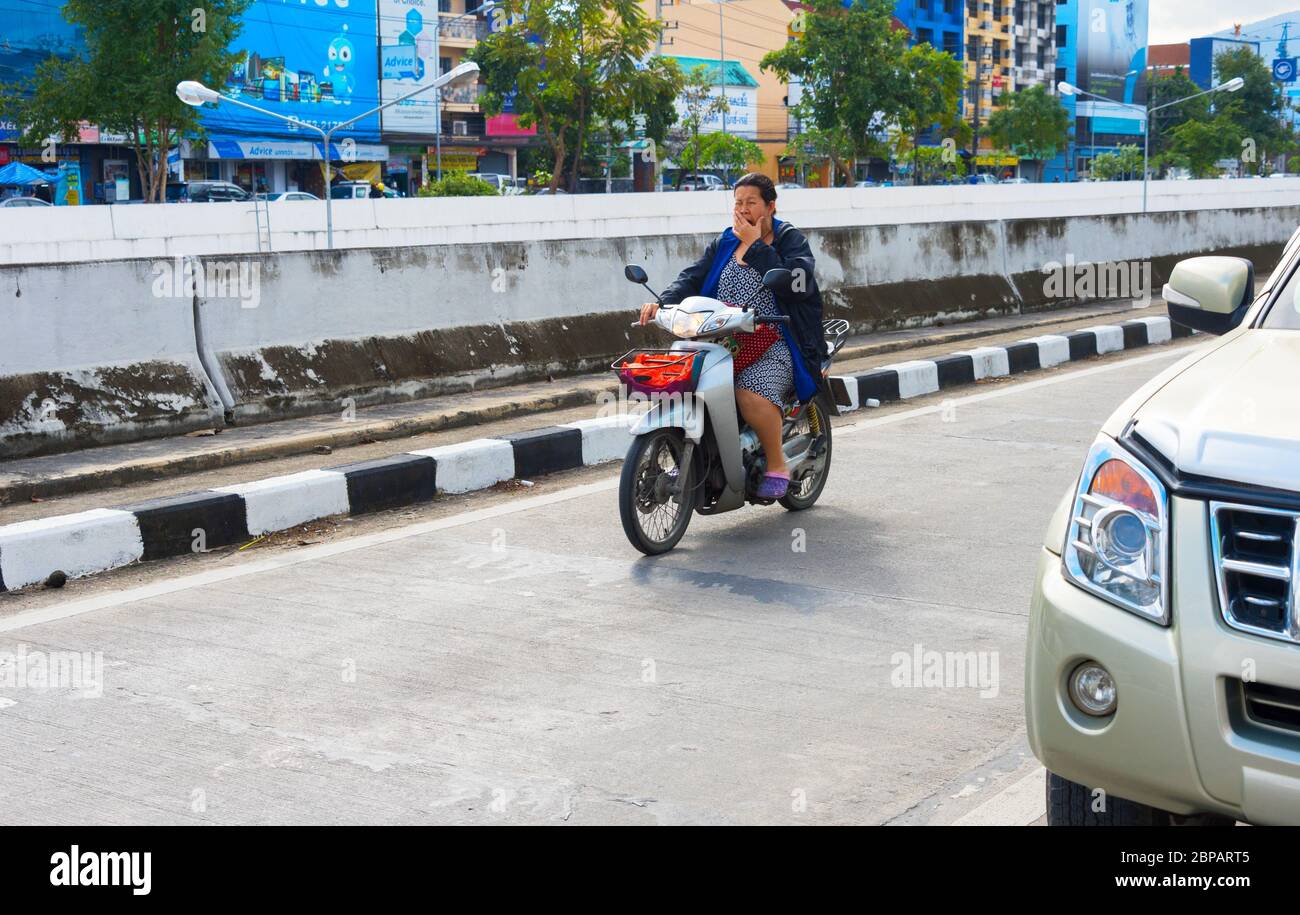 CHIANG MAI, THAILAND - 12. JANUAR 2017: Frau gähnt, als sie im Straßenverkehr ein Motorrad fährt. Stockfoto