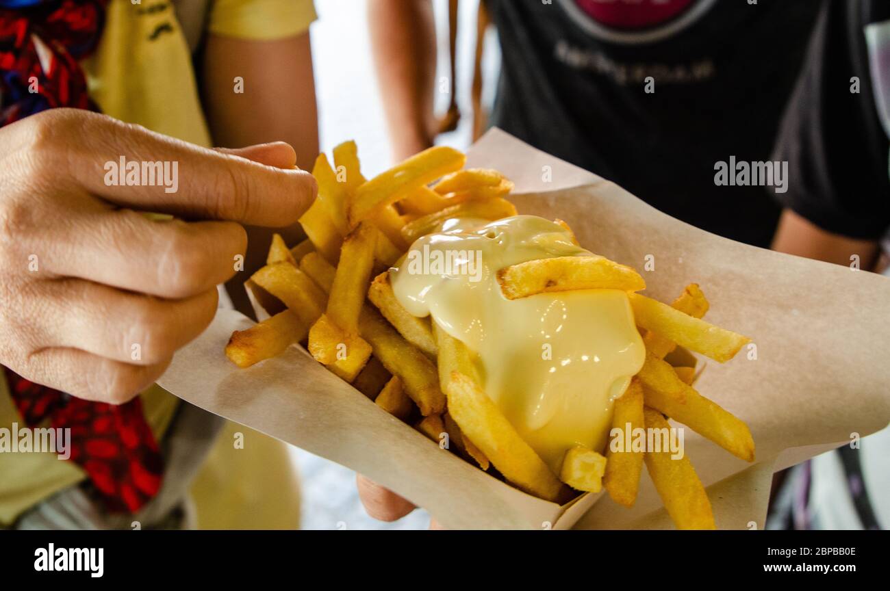 Antwerpen, Flandern, Belgien. August 2019. Eine belgische Spezialität: Pommes Frites garniert mit Sauce. Die Hand taucht einen Kartoffelchip in die Sauce, bevor sie eatin Stockfoto