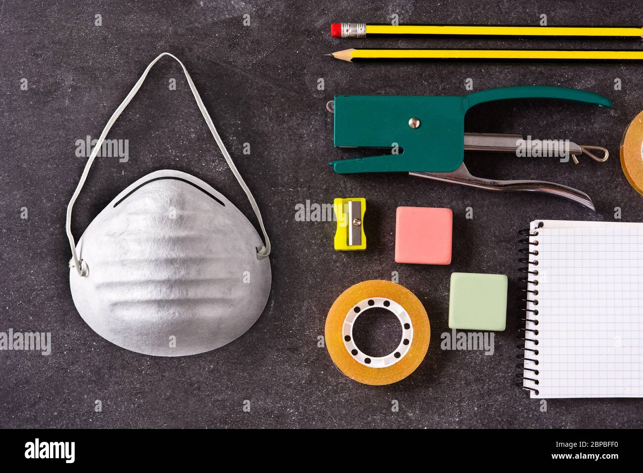 Verschiedene Schulbedarf und Schutzmaske auf schwarzem Schiefer. Zurück zur Schule Konzept. Stockfoto