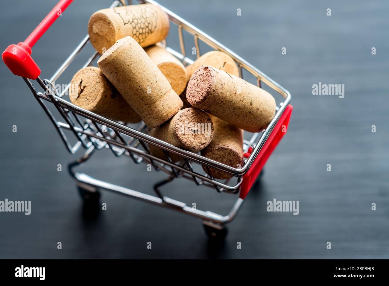 Gebrauchte rote Rebkorken im Einkaufswagen auf schwarzem Backgroiund aus Holz. Einkaufsalkoholkonzept mit Kopierraum Stockfoto