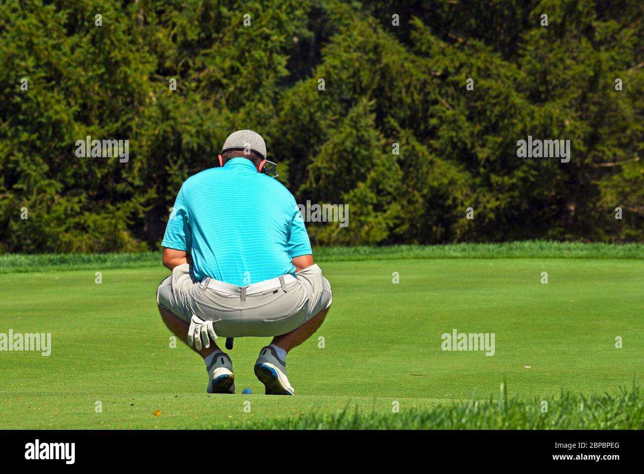 Junger Mann, der über das Grün schaut, bevor er einen Golfball setzt Stockfoto