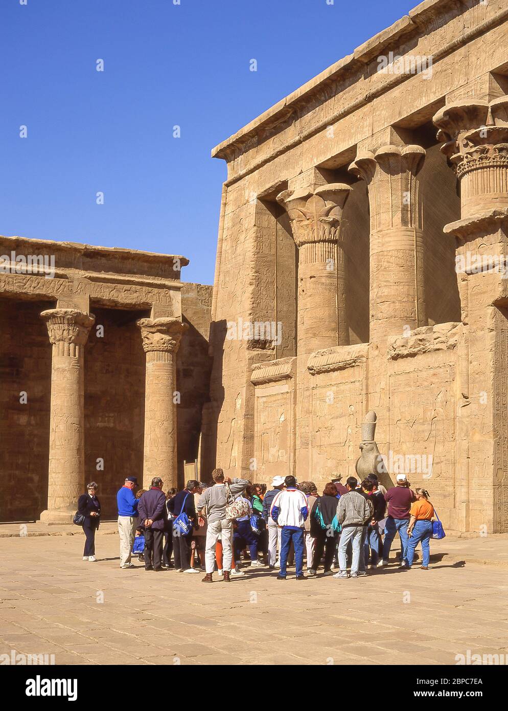 Tour-Gruppe mit Guide durch die Statue von Horus im Hof des Tempels von Horus, Edfu, Assuan Governorate, Ägypten Stockfoto