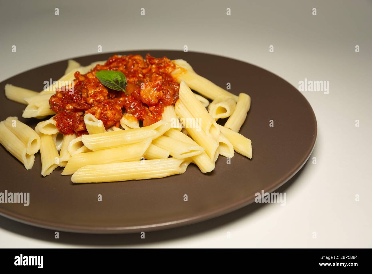 Pasta und Hackfleisch mit Sauce auf einem braunen Teller auf weißem Hintergrund Stockfoto