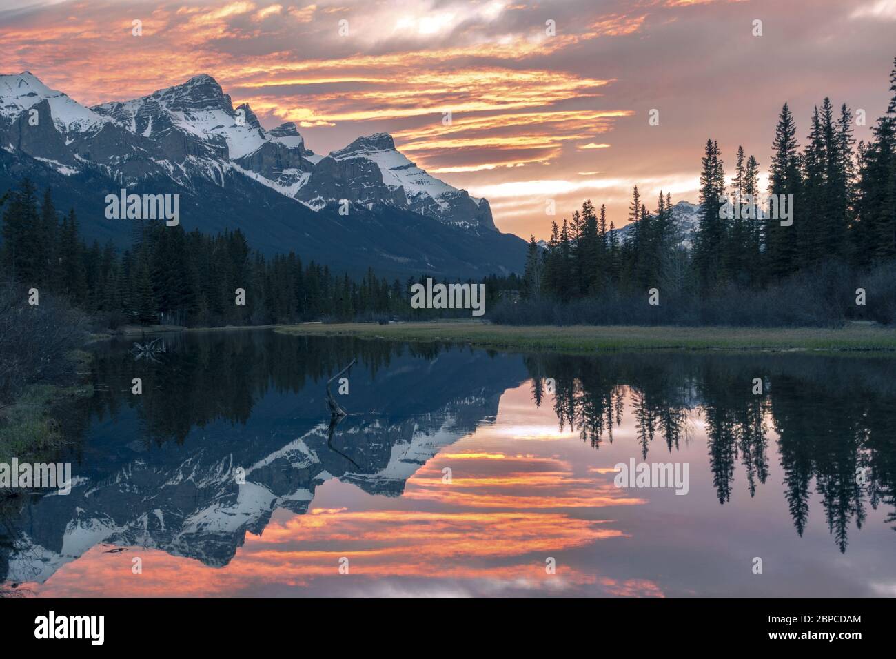 Szenischer Sonnenuntergang Abendfarben Canmore Spring Creek Mountain Village und entfernte verschneite Rocky Mountain Peaks Landschaft, Frühfrühling, Alberta Kanada Stockfoto