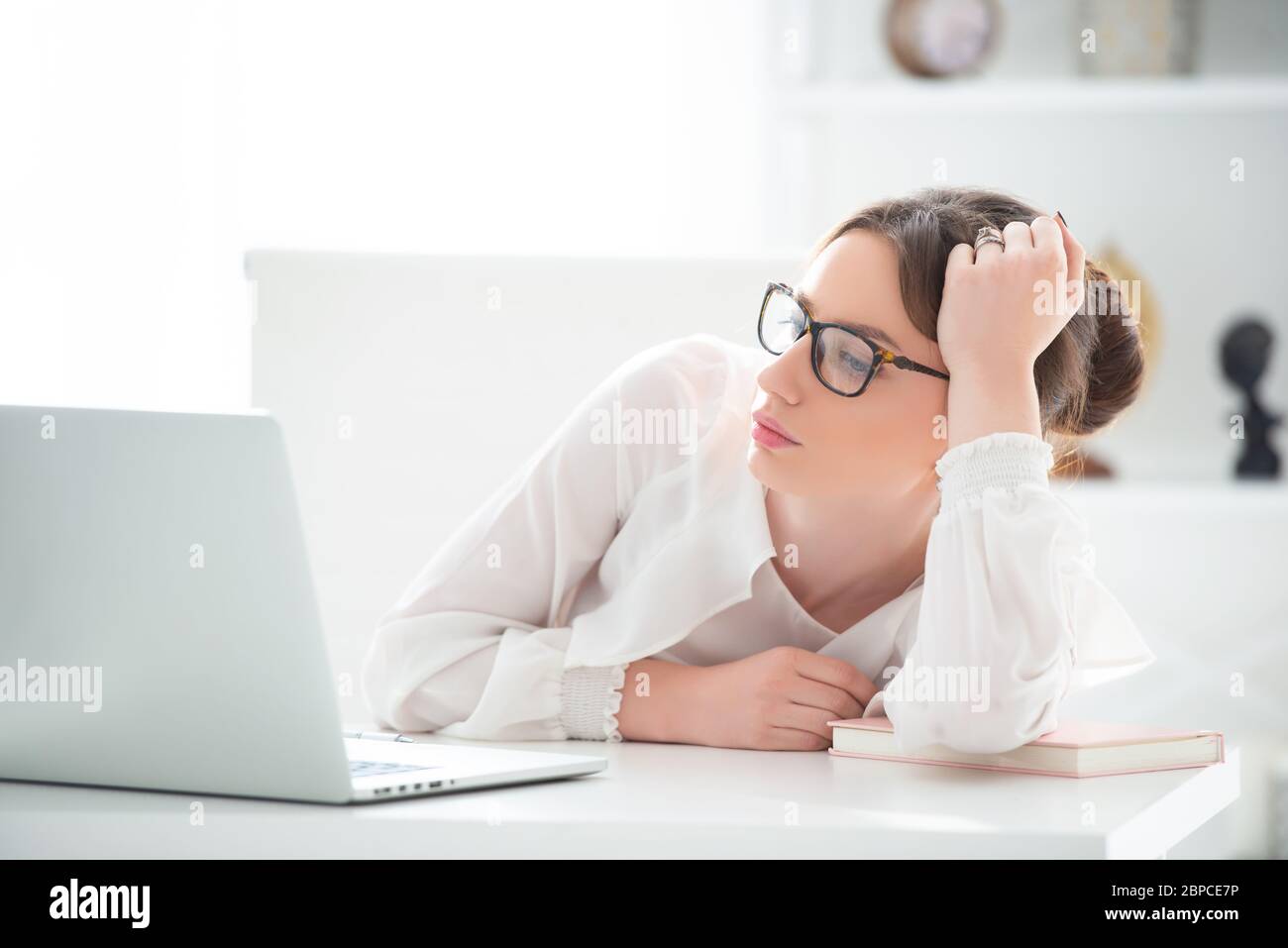 Eine verärgerte junge Frau sitzt in einem Büro an einem Laptop und hält ihren Kopf in den Händen. Probleme bei der Arbeit Stockfoto