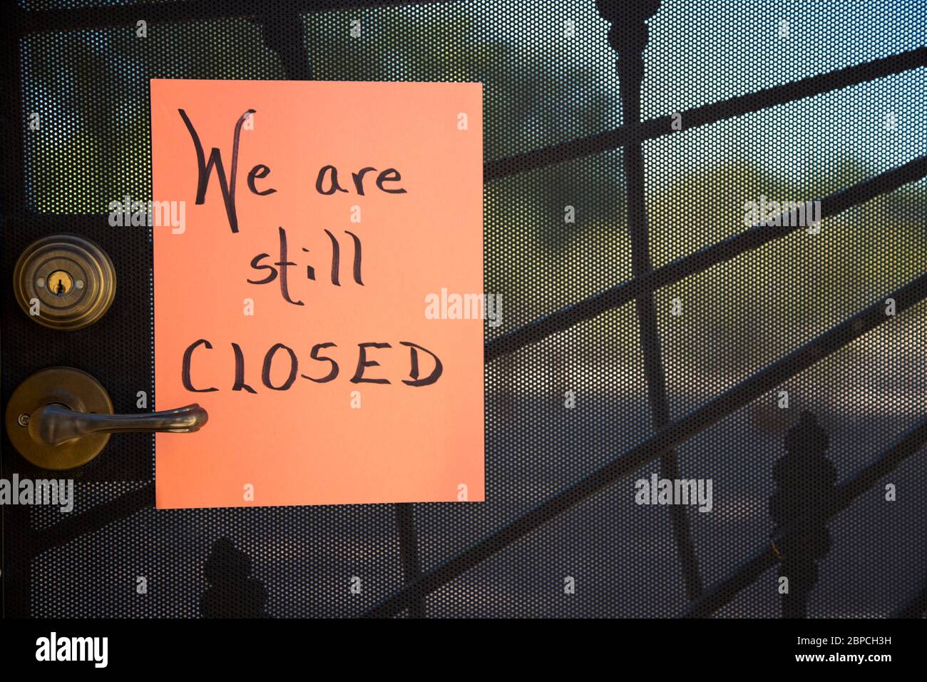 Schwarzes Stahlgitter mit Schloss und Griff ist Hintergrund für handgeschriebene Wir sind noch GESCHLOSSEN Schild auf orangen Papier Stockfoto
