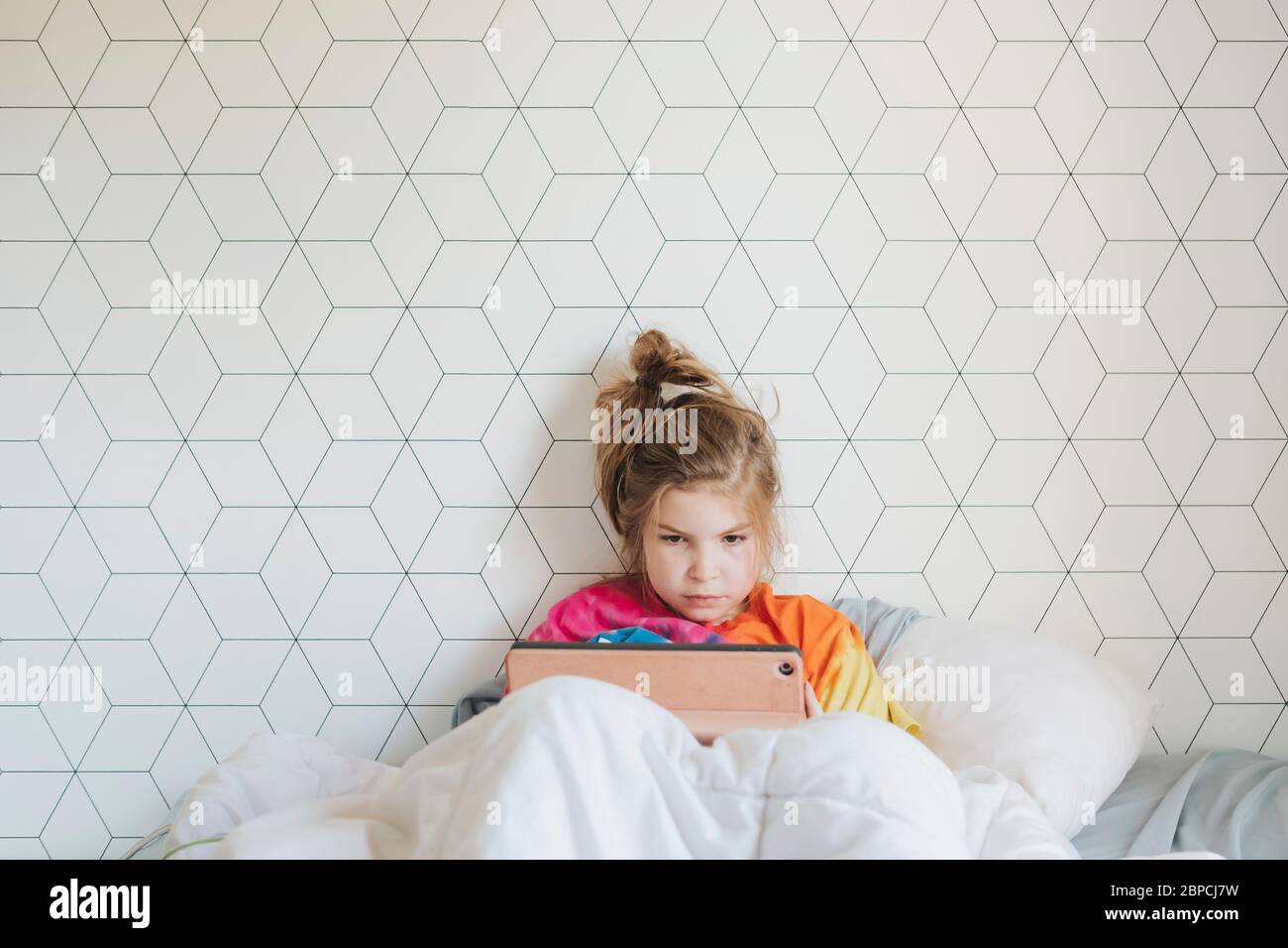 Junges Mädchen im Bett sitzend, das ihr digitales Gerät anschaut Stockfoto