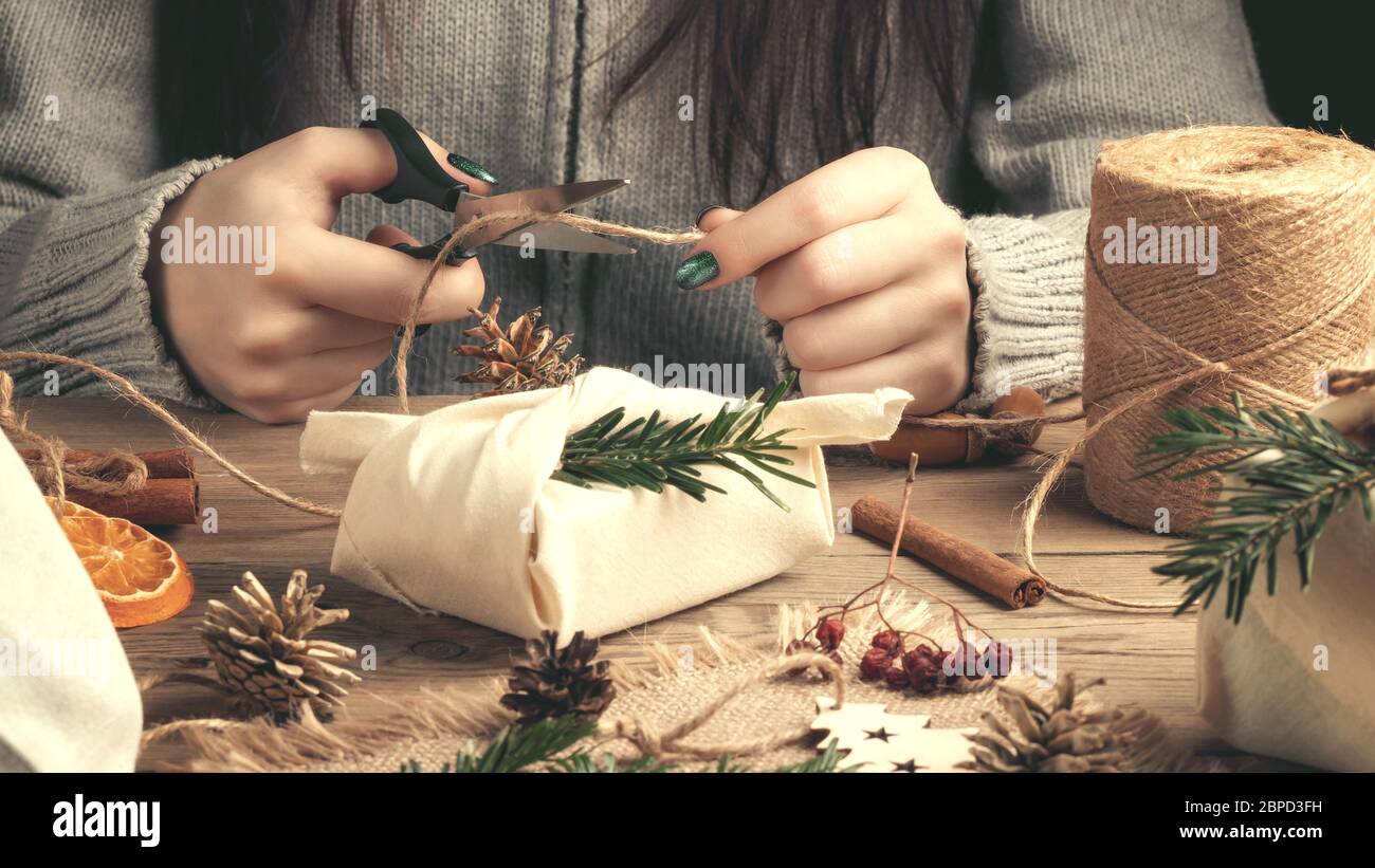 Null Abfall und umweltfreundliches weihnachtskonzept. Weibliche Hände wickeln Geschenke in Naturstoff mit Ornamenten aus natürlichen Materialien. Stockfoto