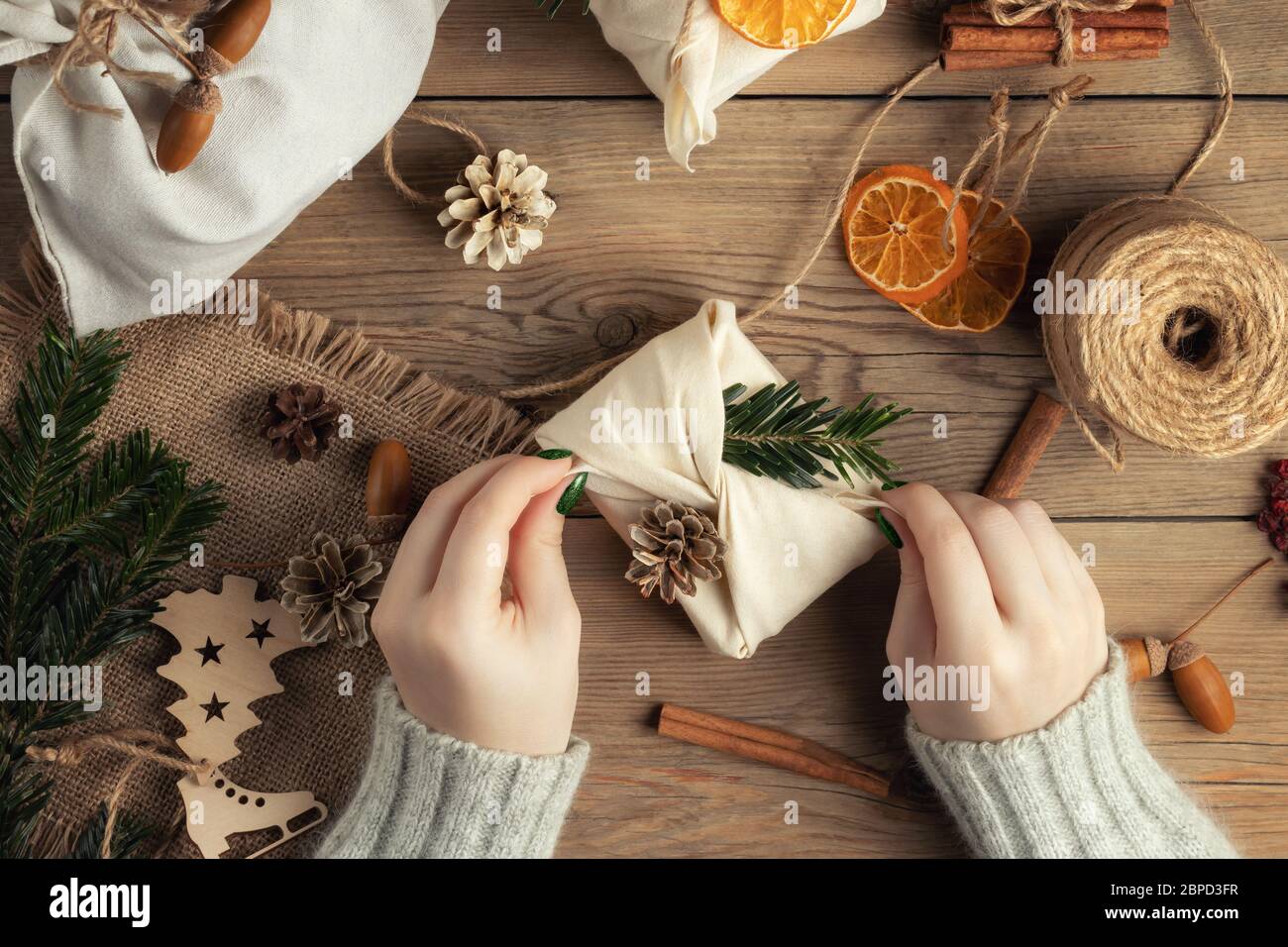 Zero Waste und umweltfreundliches weihnachtskonzept. Weibliche Hände wickeln Geschenke in Naturstoff mit Ornamenten aus natürlichen Materialien, Draufsicht, flach legen Stockfoto
