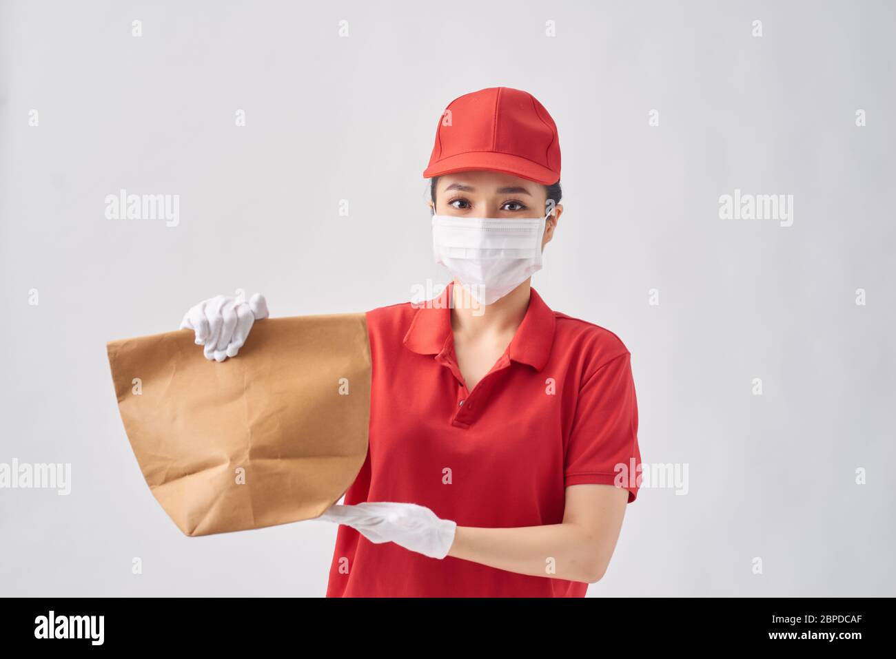 Gesundheitsschutz, Sicherheit und Pandemie Konzept - Lieferung Frau in schützende Gesichtsmaske mit Lebensmitteln in Papiertüte auf rosa Hintergrund Stockfoto