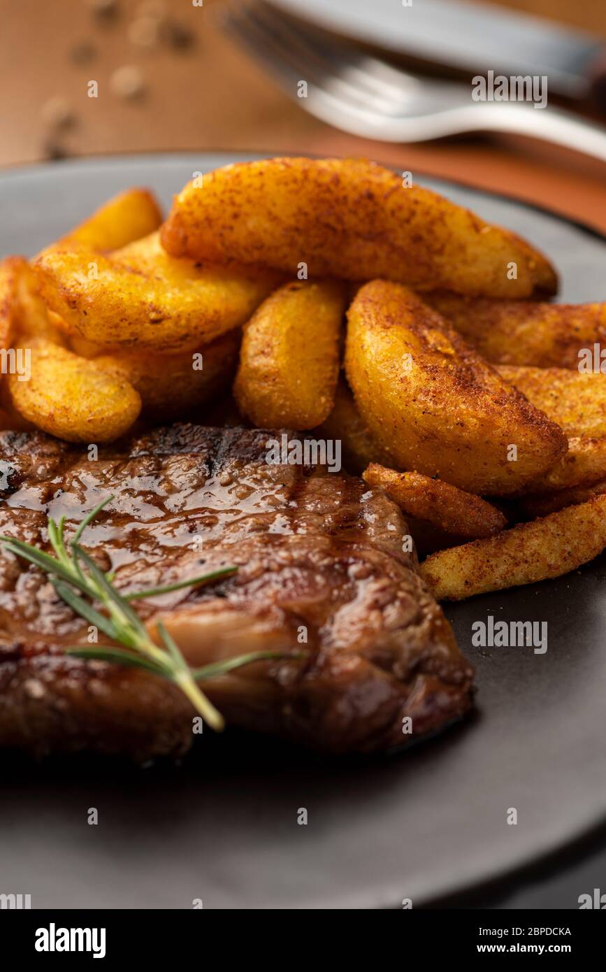 Steak mit goldenen würzigen Pommes Frites und Rosmarin ein schwarzer Keramikplatte mit Weingläsern Serviettenleder Matte und Paprika Stockfoto