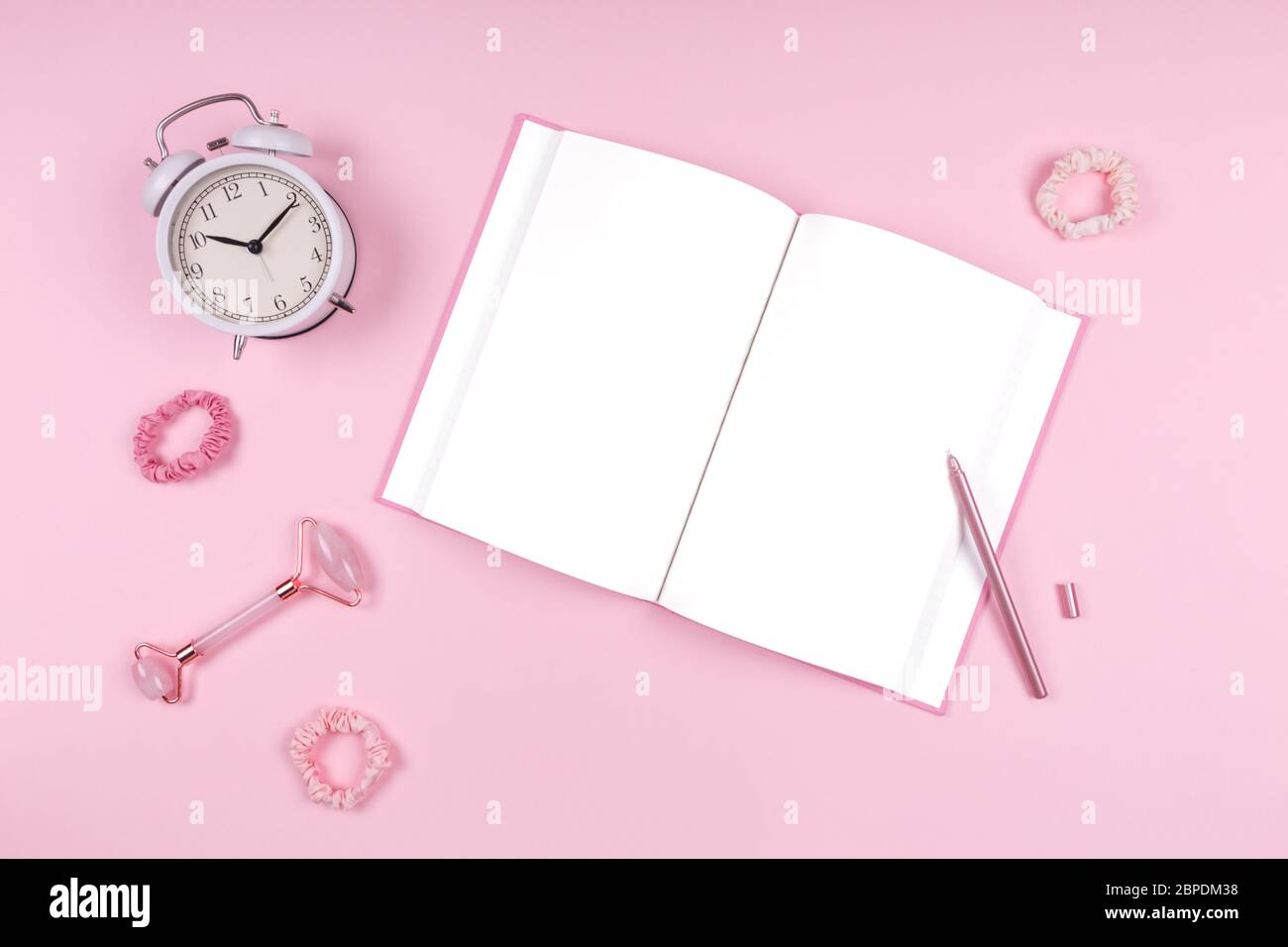 Tagebuch mit stilvollem Stift, Jade Face Roller, weiße Uhr und rosa Accessoires. Beauty Time, Selfcare und Beauty Accessoires Konzept. Platz für Text Stockfoto