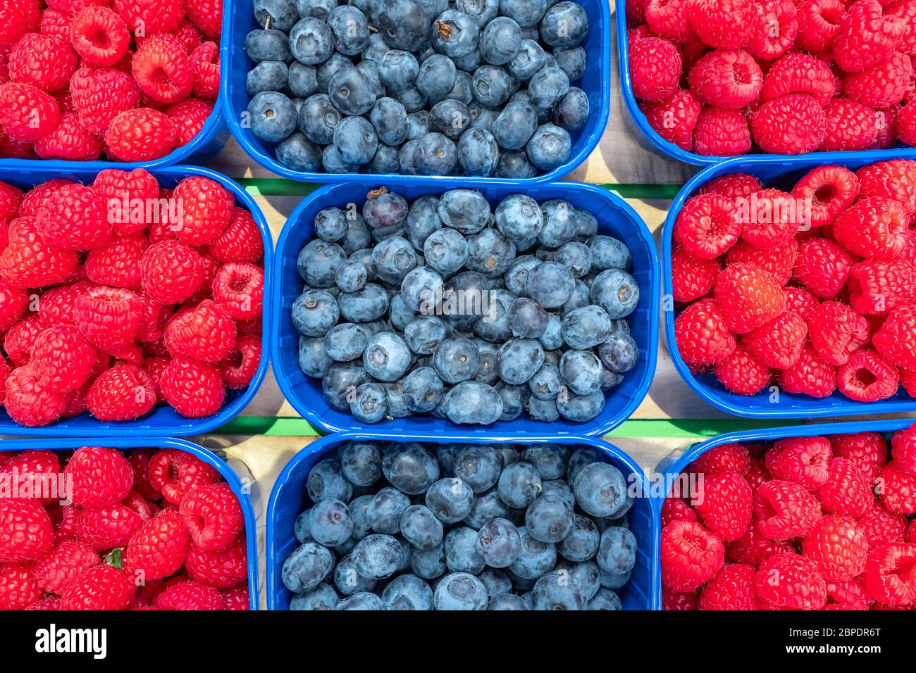 Heidelbeeren und Himbeeren in blauen Kisten auf dem Lebensmittelmarkt. Stockfoto