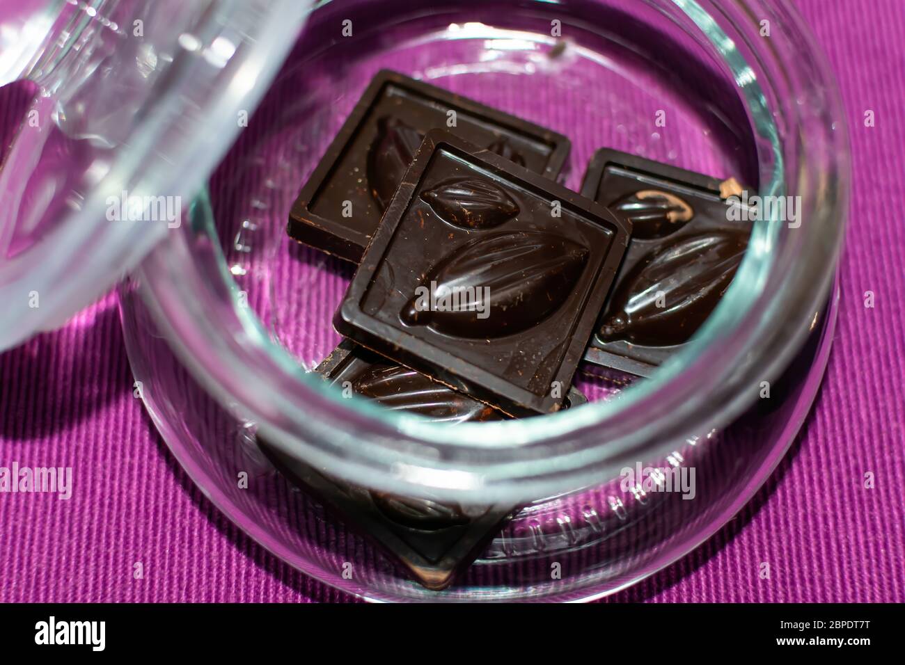 Stücke von handgefertigten Schokolade sind in einem Glas auf einem lila Hintergrund, close-up, selektive Fokus. Nützliche und leckere Süßigkeiten. Stockfoto