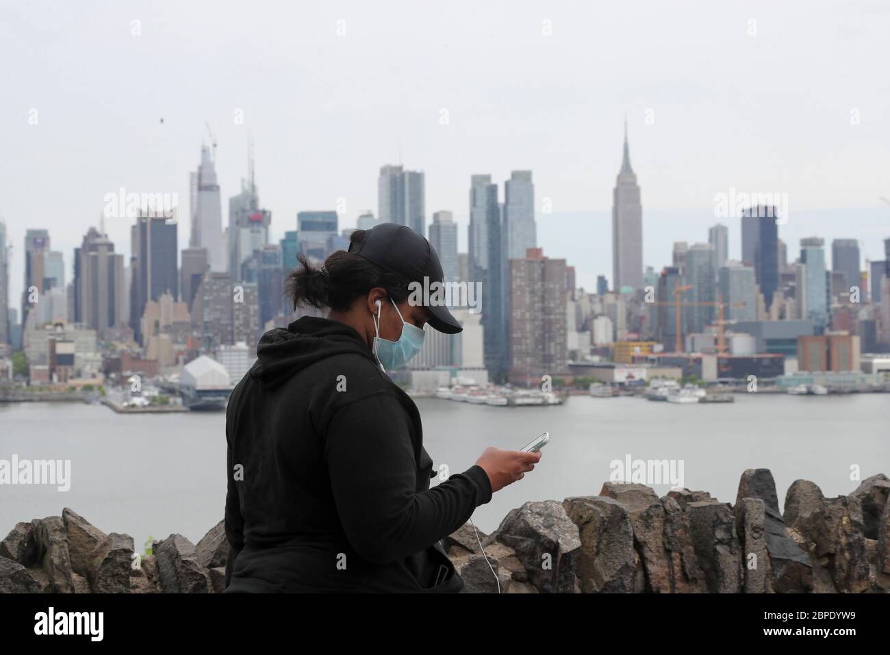 New York, USA. Mai 2020. Eine Frau mit Gesichtsmaske geht in der Nähe des Hamilton Parks mit der Skyline von Manhattan im Hintergrund in Weehawken von New Jersey, USA, am 18. Mai 2020. Die Anzahl der COVID-19-Fälle in den Vereinigten Staaten überstieg 1.5 Millionen am Montag, erreichte 1,500,753 von 16:03 Uhr (2003 GMT), nach dem Center for Systems Science and Engineering (CSSE) an der Johns Hopkins University. Die nationale Todesrate von COVID-19 stieg laut CSSE auf 90,312. Kredit: Wang Ying/Xinhua/Alamy Live News Stockfoto